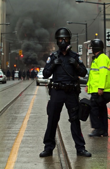 Police officer blocks people from passing at the Toronto G20 while police car is on fire in the background - Photographed by Peter Gatt - PHOTO101.CA